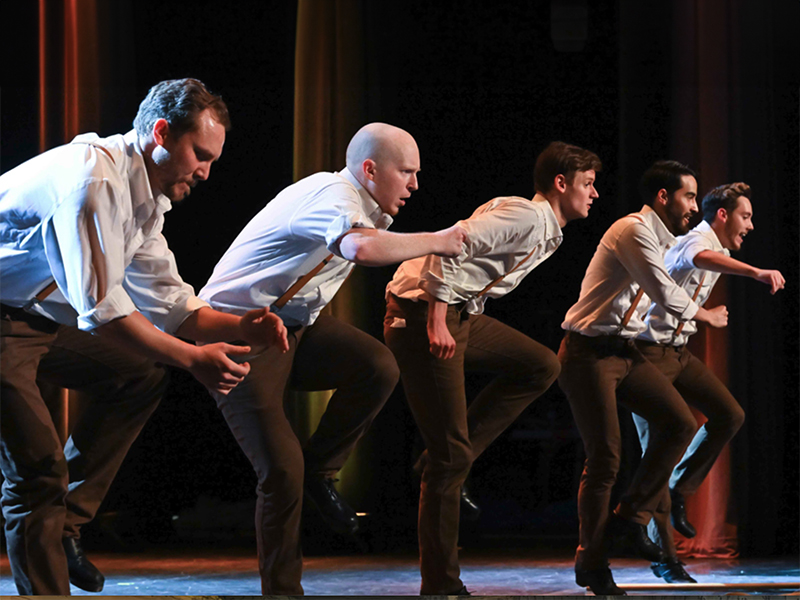 Four men in black pants and silky shirts perform an Irish step dancing routine 