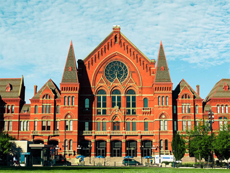 A painting of the front of the Cincinnati Music Hall with a bright blue sky overhead and warm green grass in front 