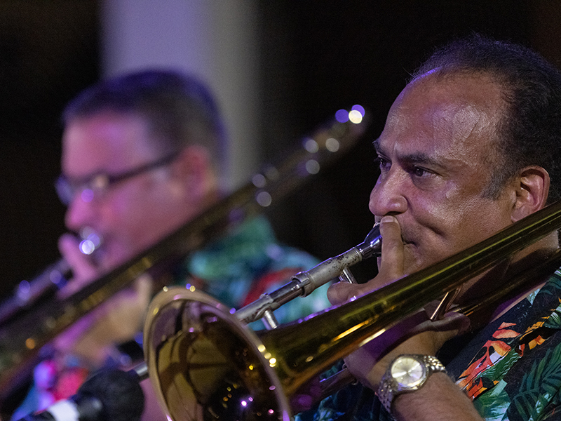 Two Latino Men playing brass instruments in teal and fuschia hawaiian style shirts