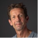 Headshot of an older man with a long face and short brown hair faintly smiling