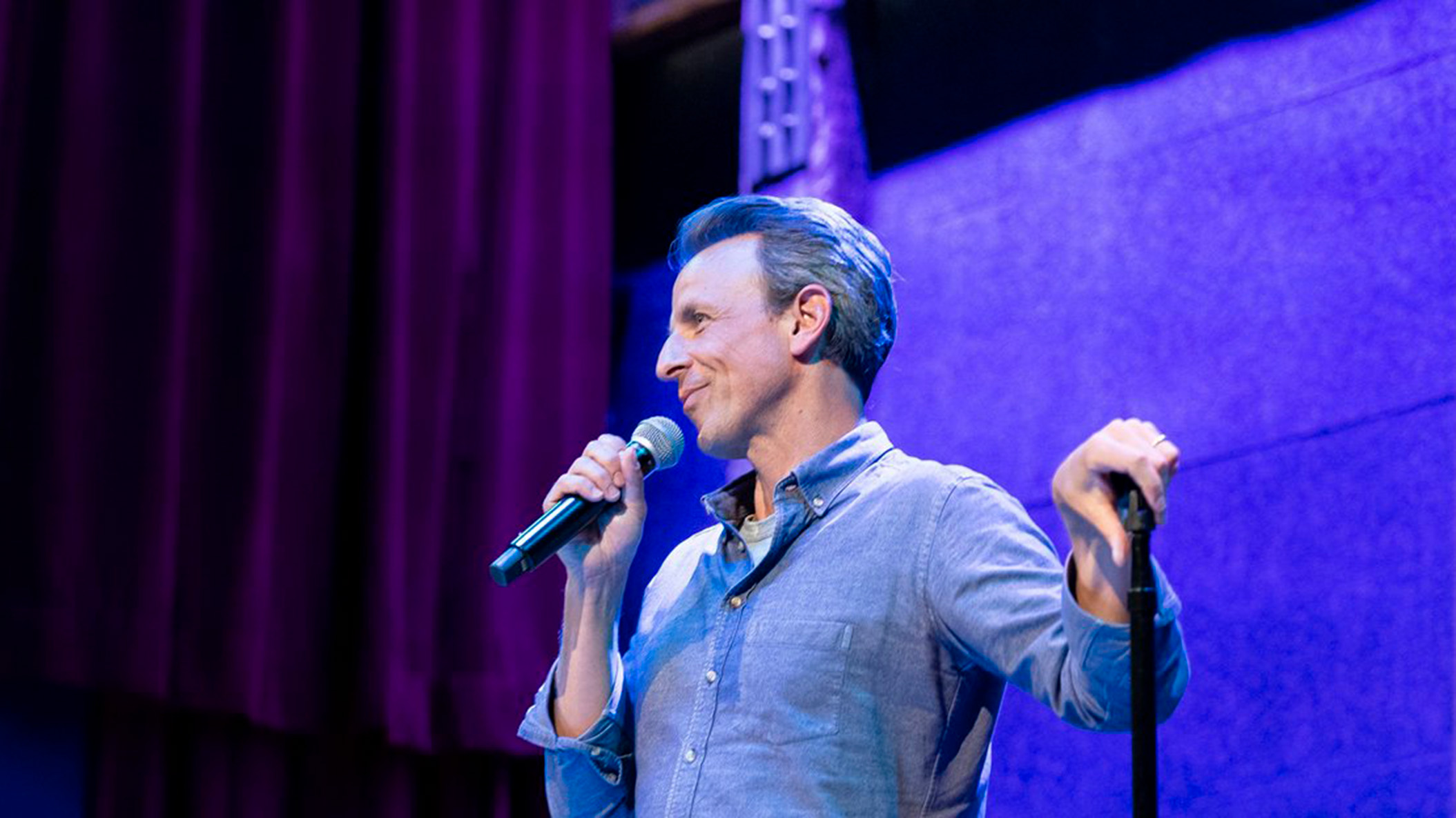 Photo of a man with salt and pepper hair standing holding a microphone 