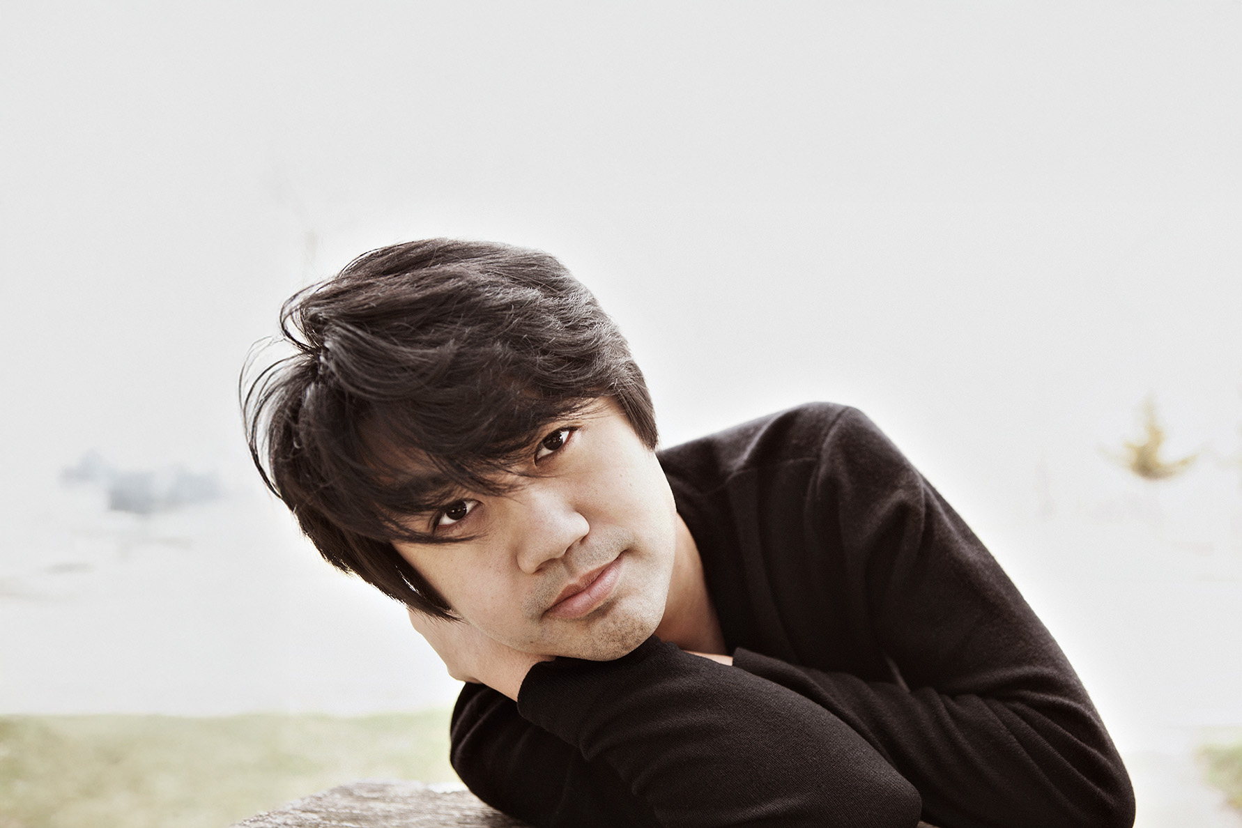 professional headshot of a man with dark hair and eyes looking directly into the camera with his head resting on his arm  in a relaxed pose