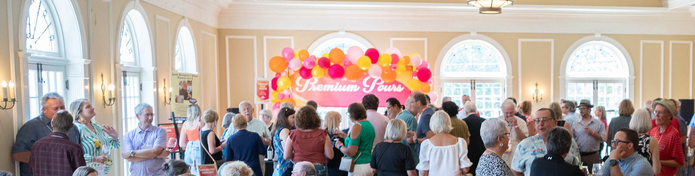 A photo of many people gathered in the light filled ballroom of the Oxford Community Arts Center with chatting and having a good time