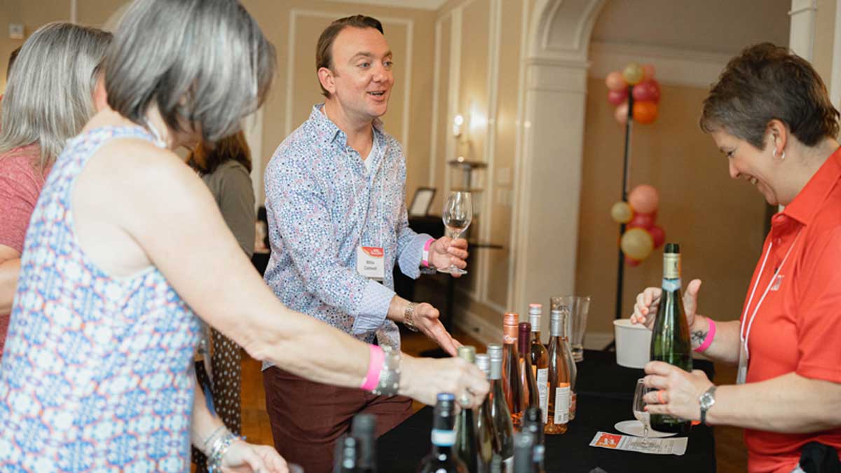  Several attendees inspect bottles of wine while a volunteer offers another pour