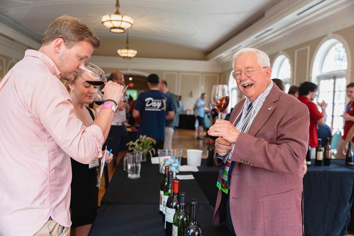 Miami University alumni tasting and discussing wine with Jack Keegan at a wine tasting event table in the Oxford Community Arts Center.