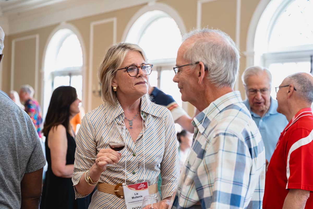 Liz Mullenix conversing with an attendee and enjoying wine at a wine tasting event in the Oxford Community Arts Center.