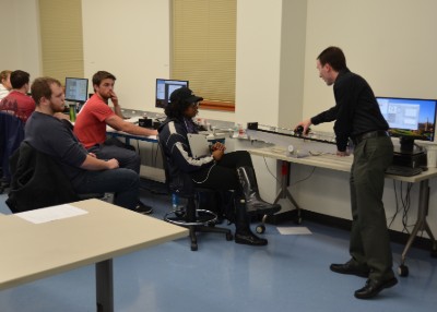 A faculty member talks with students working at computers