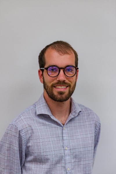 Dr. Mark Sidebottom, in a plaid shirt, posing/smiling in front of a white wall