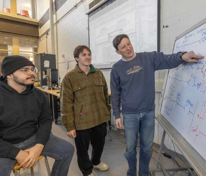 Professor talking to 2 students at a whiteboard dueing the SASI workshop
