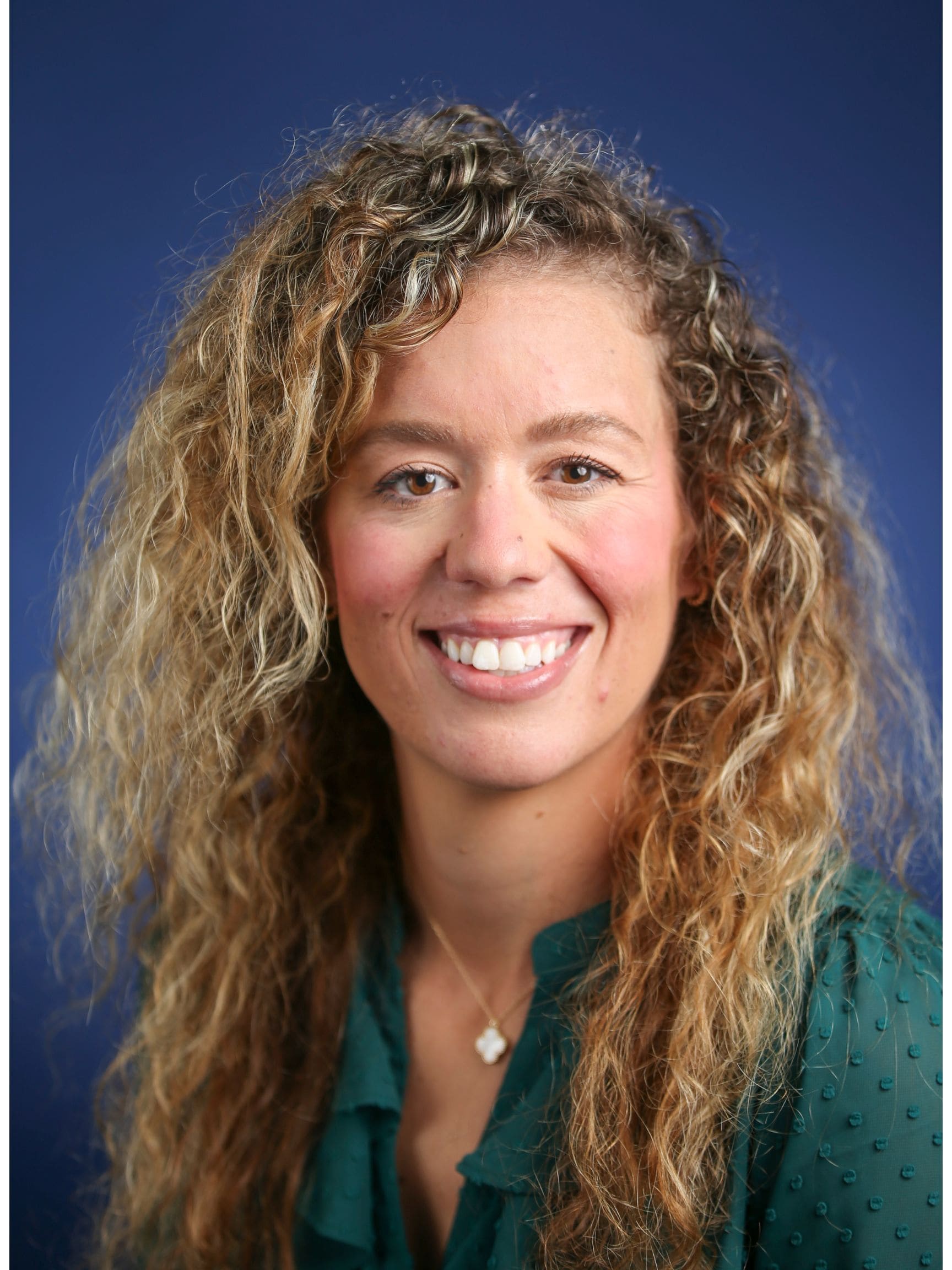 Smiling woman with long curly hair in a studio headshot against a blue background.