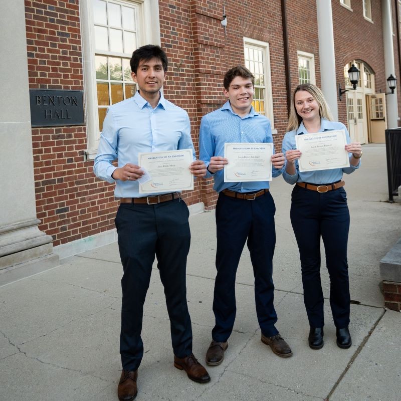 Three male student standing outside Benton Hall holding Order of the Engineer Ceremony certificates.