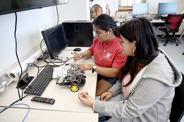 A pair of female electrical engineering students work on connecting wires in a miniature vehicle