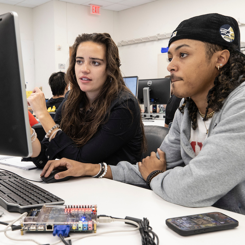 A male and female student communicate and collaborate on an electrical engineering assignment.