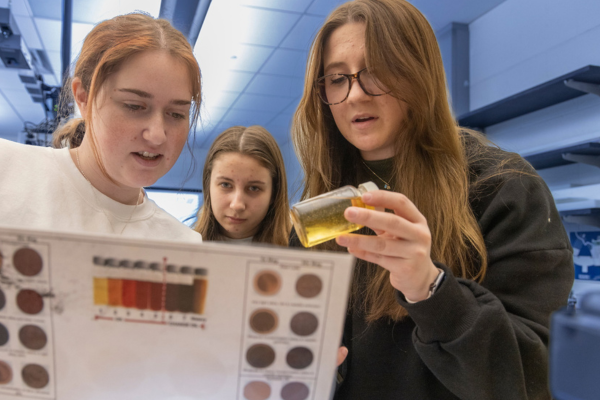 Three female CEC students closely inspect a manufacturing process during a reliability training workshop.