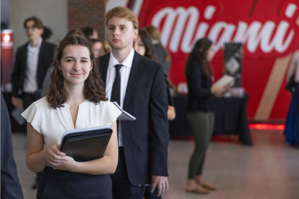 Female CEC student smiles at camera with binder in hand at career fair.