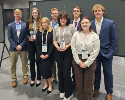 Students Felicia Guagliardo and Grace Kemmerly hold the awards they won and smile and pose with CEC professor Andrew Jones and the other students who attended the conference: Nolan Brown, Philip Glave, Brooklyn Lengyel, Brynley Platt, and Jonathan Ackley.