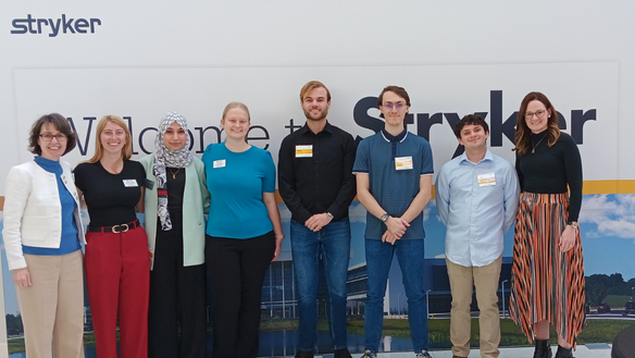 A group of biomedical engineering students in front of Stryker signage on an industry visit