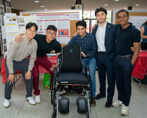 Five engineering students smile and pose around a uniquely engineered wheelchair.