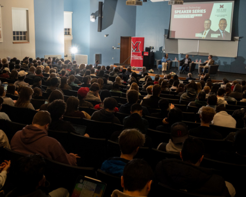 Picture shows large audience in Benton Hall auditorium and speakers on stage.