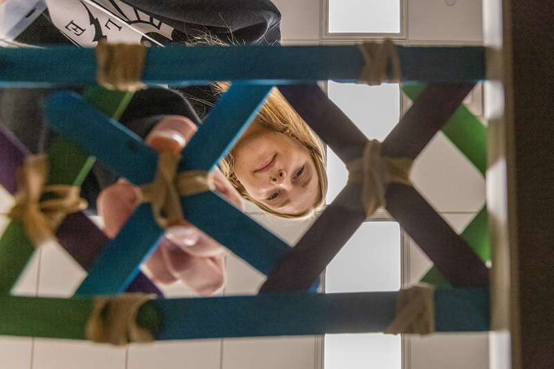 Student looks down viewing her bridge made of popsicle sticks.