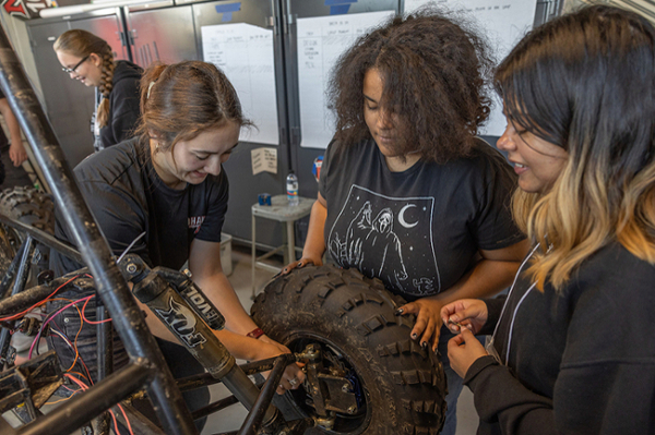 Multiple students work to fix the bottom half of a car during the RedHawk Racing session.