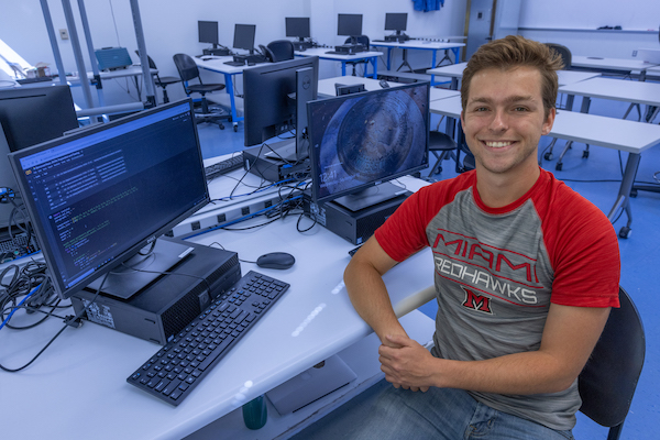 CEC Graduate Student Tyler Gandee sits in front of a computer monitor with code