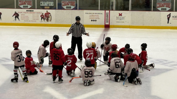 Peter Jamieson in hockey referee uniform with youth hockey team assembled around him on the ice