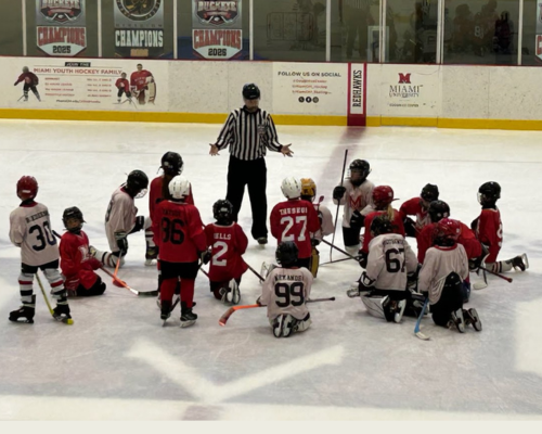 Peter Jamieson in hockey referee uniform with youth hockey team assembled around him on the ice
