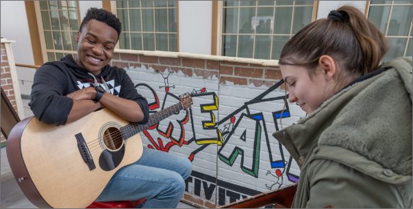 two students playing acoustic guitars together