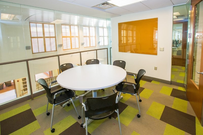 Small Meeting room with a round table, six chairs around it. Dry erase board on the wall. 