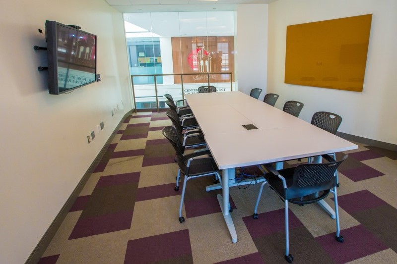 Long conference table with 12 chairs, a tv screen on one wall and a dry erase board on the other.
