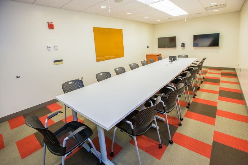 Long conference table with 16 chairs, two TVs on one wall and a dry erase board on another