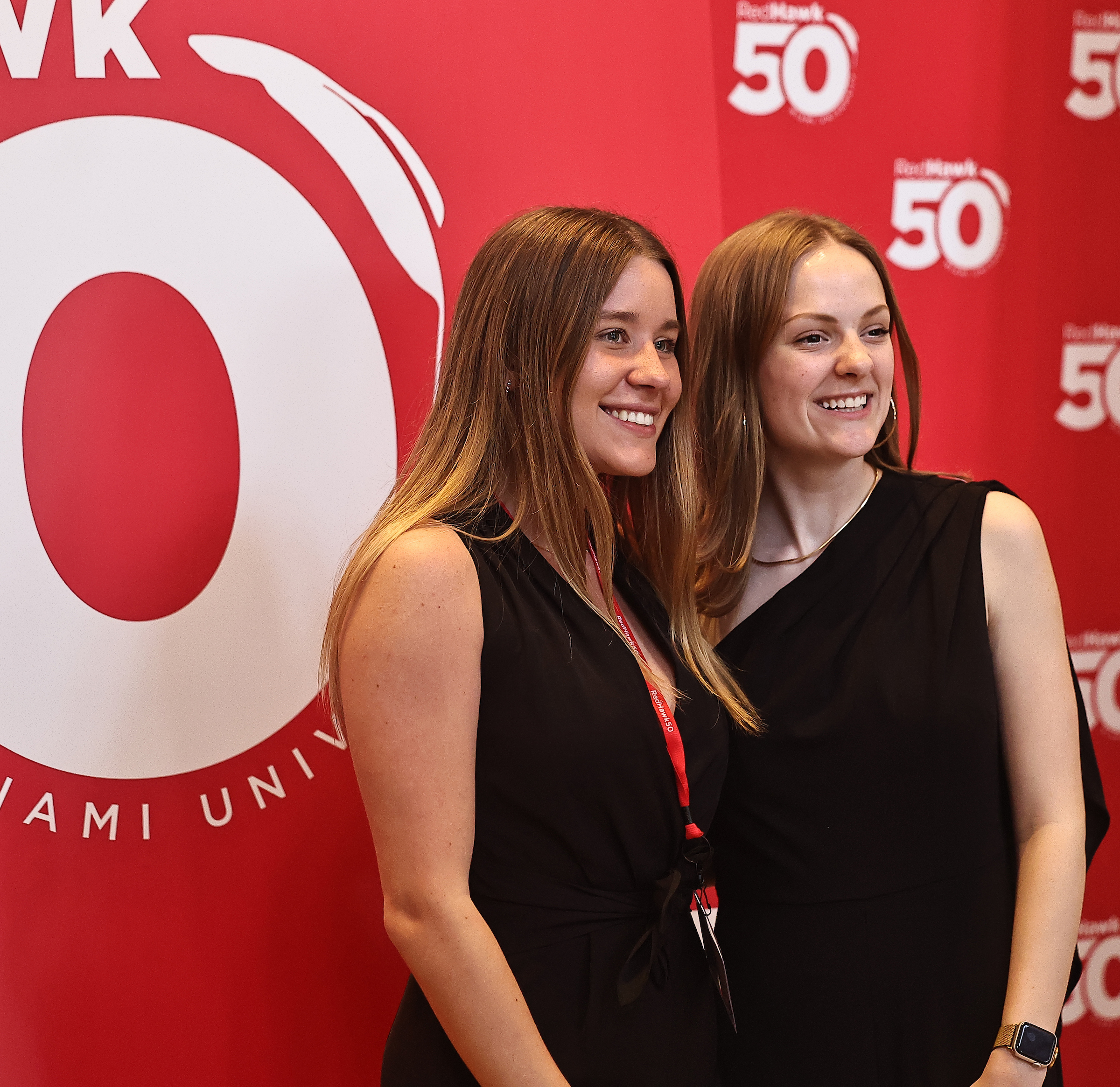 Two alumni pose for a photo in front of a RedHawks 50 backdrop.