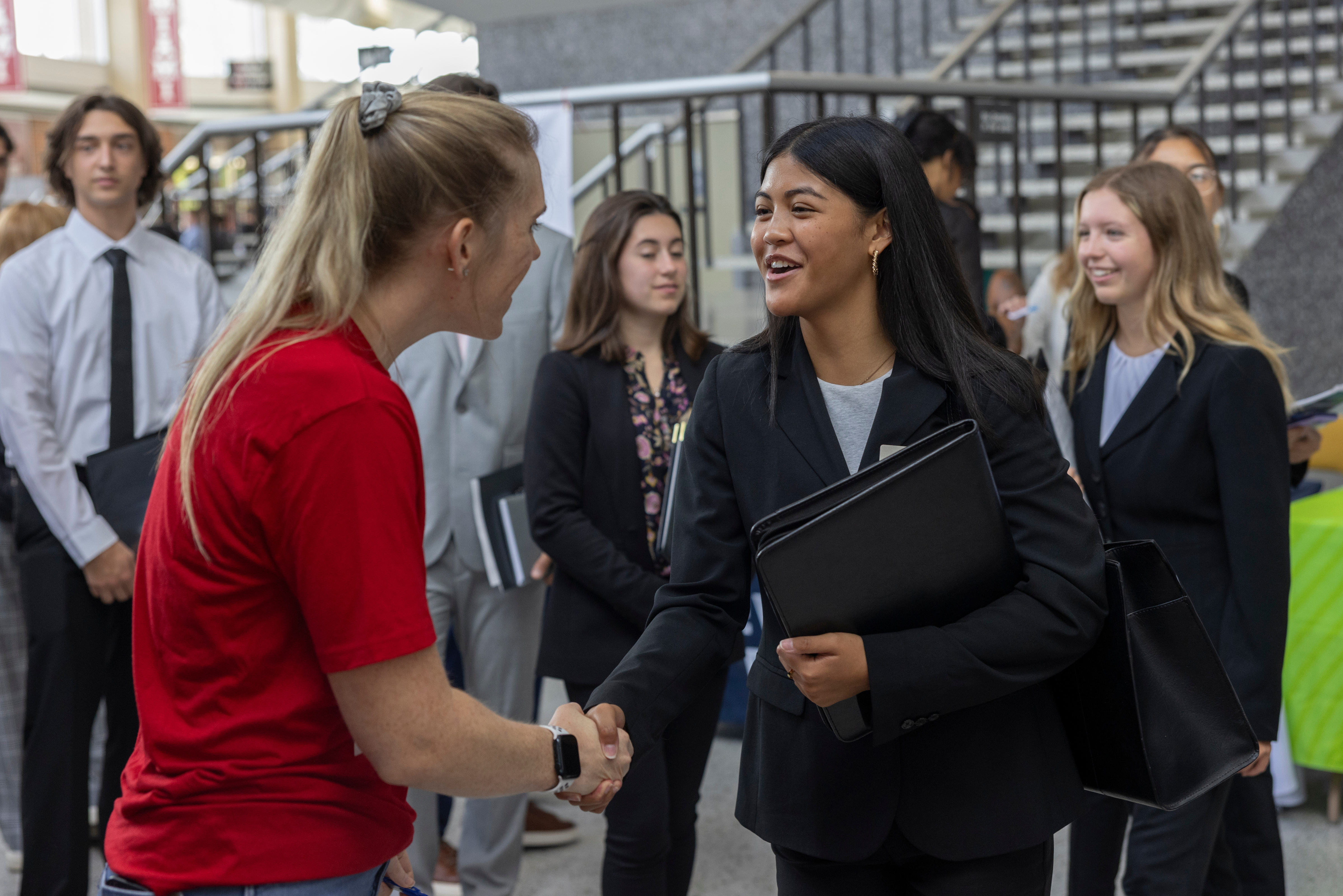 A student smiles while shaking hands with an employer at a career fair.