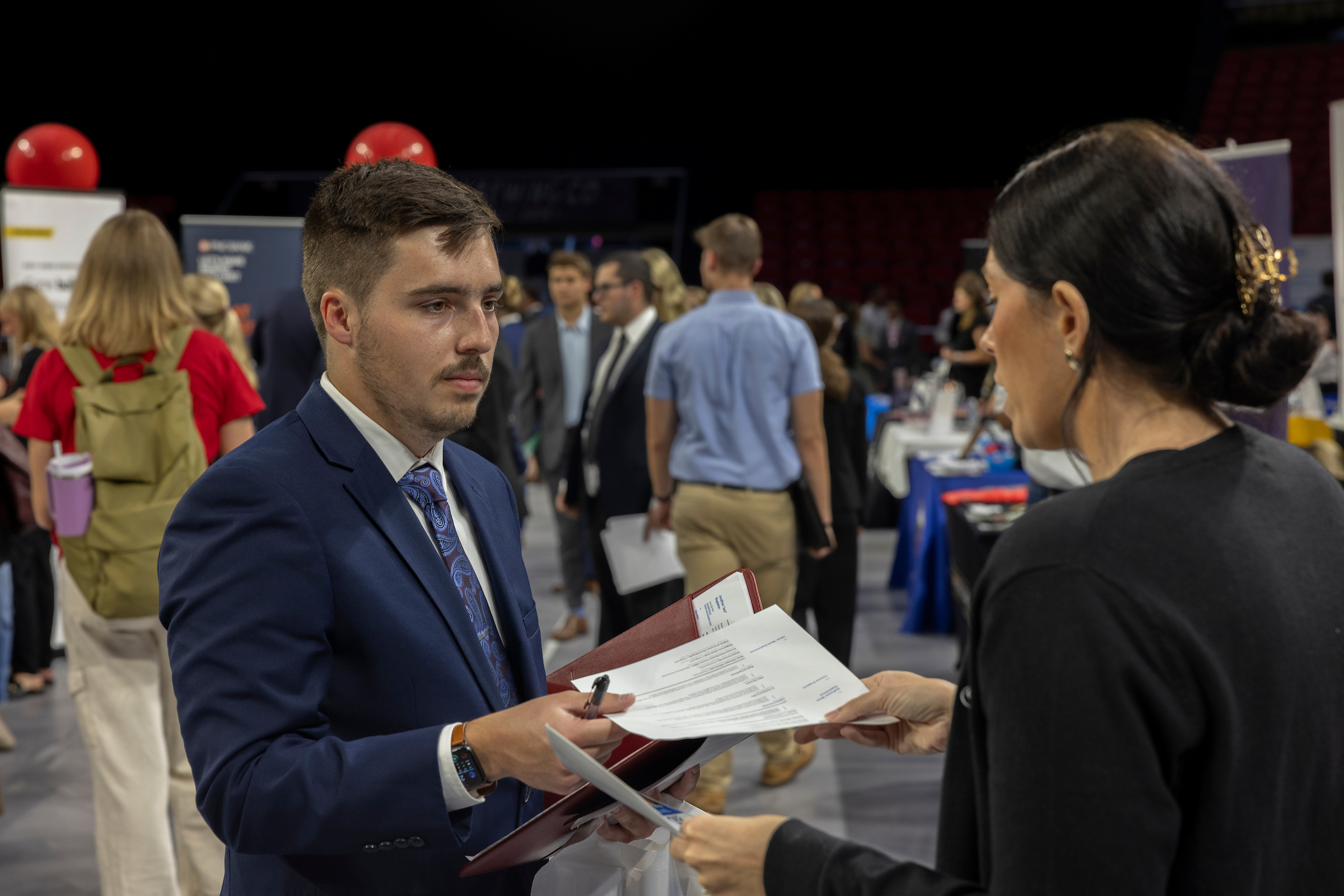A student hands an employer a resume at a career fair.