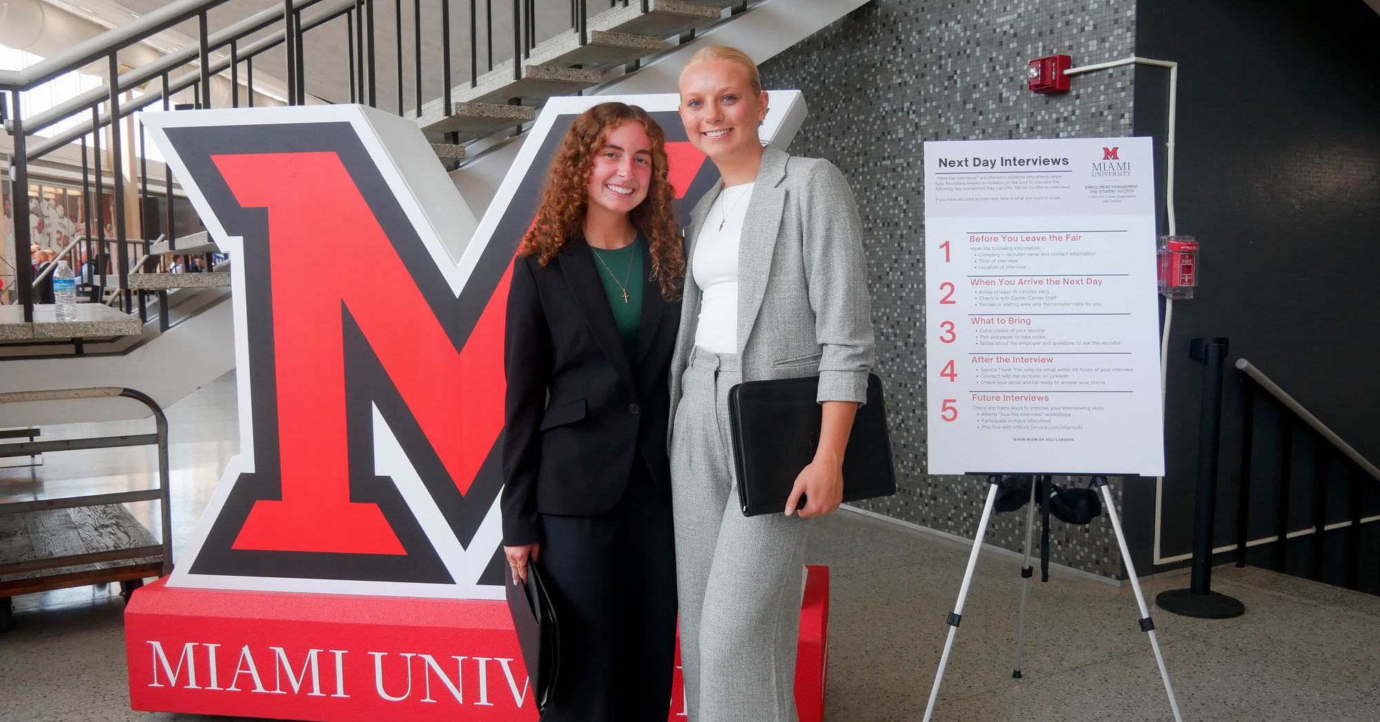 Two students pose for a picture with the block M at a career fair.