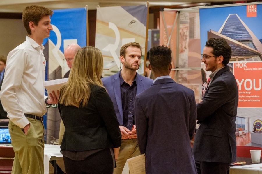 An employer speaks with a group of students at a career fair.