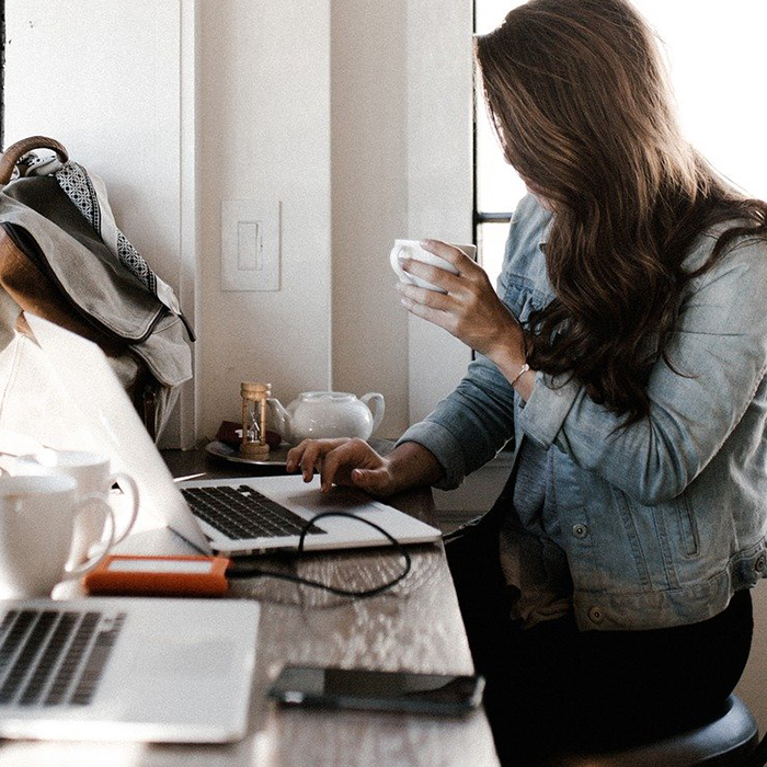 Female student working at a computer while drinking a cup of coffee