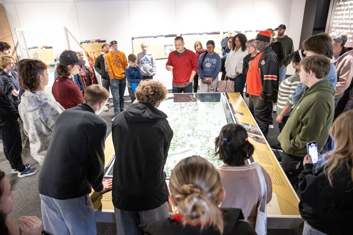 A group of students look at a map display with a professor.