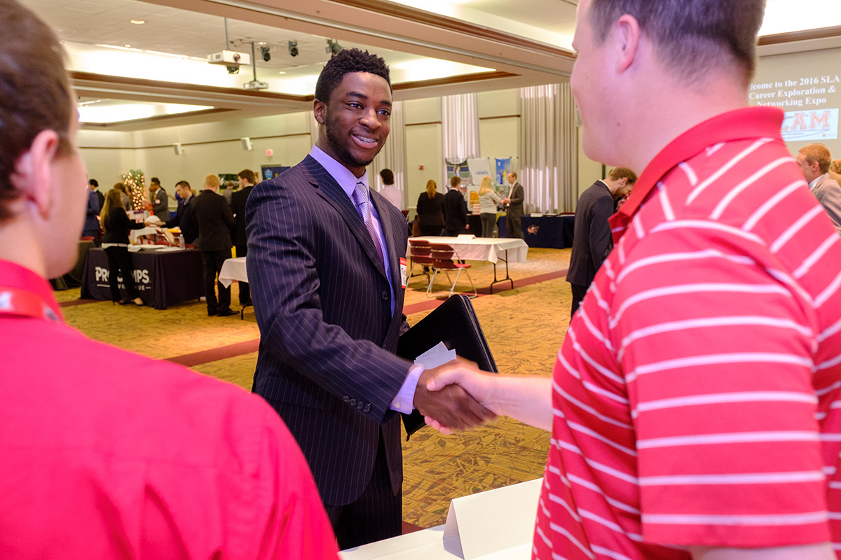 A student shakes hands with an employer at a career fair.