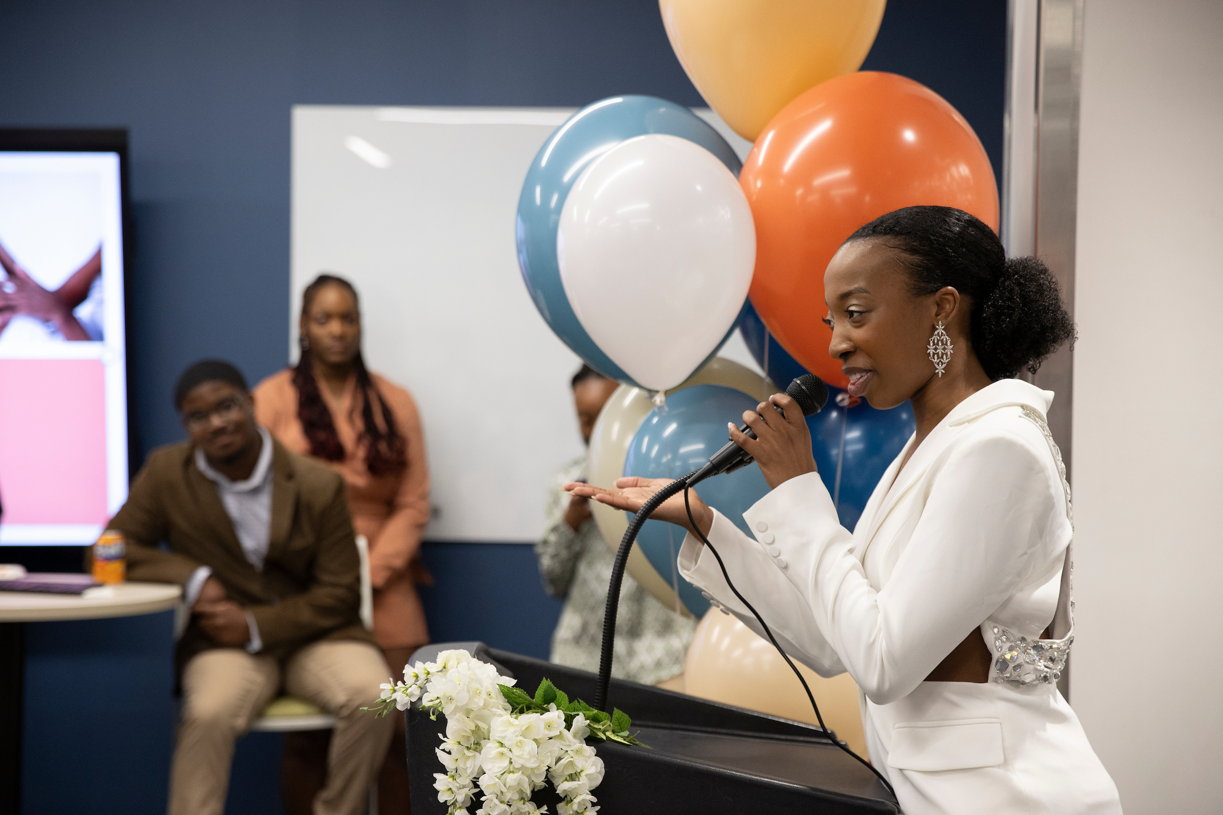 A keynote speaker addresses a crowd in front of a backdrop of balloons.