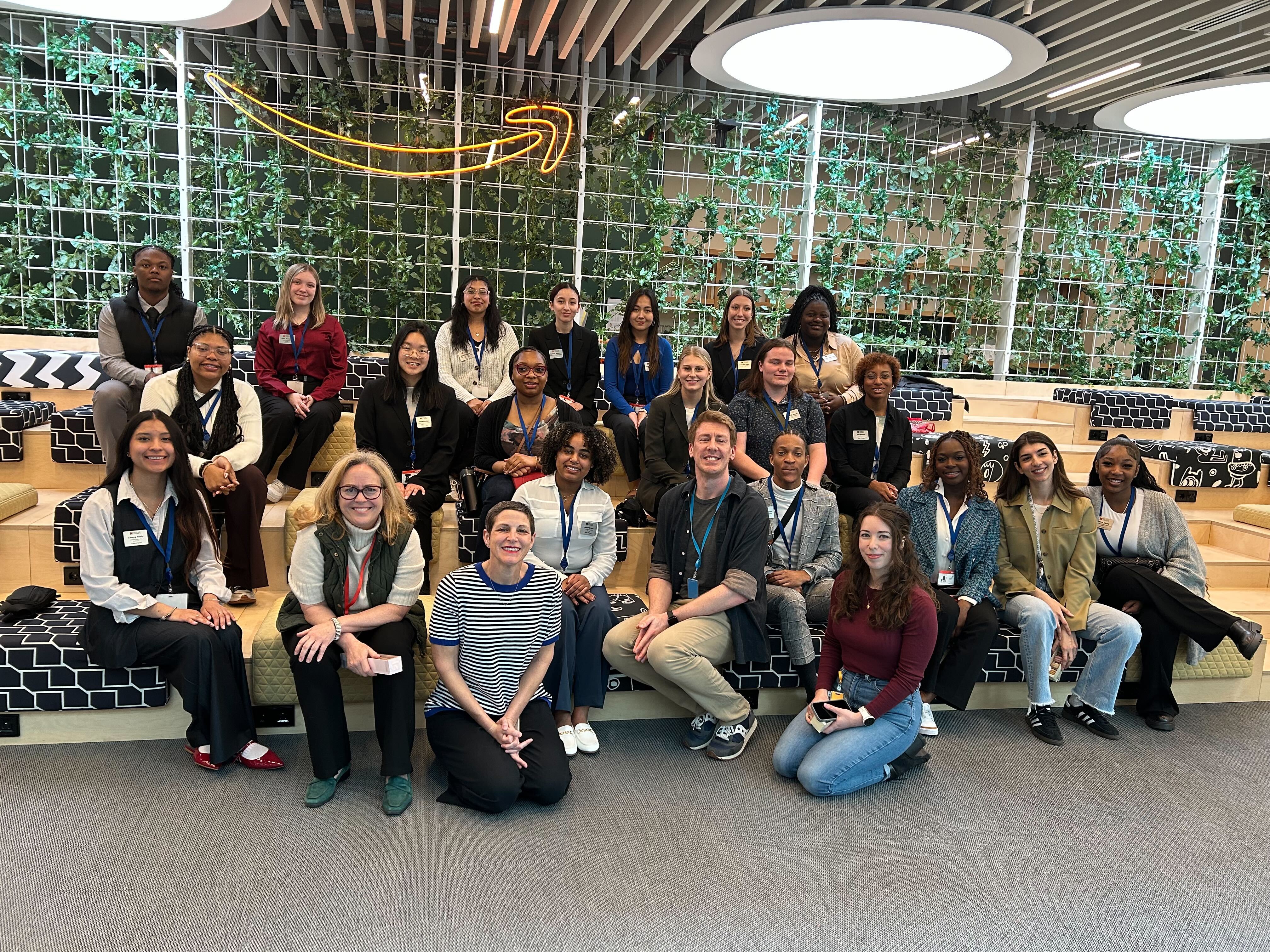 A group of students pose for a photo in front of the Amazon logo during a career trek.