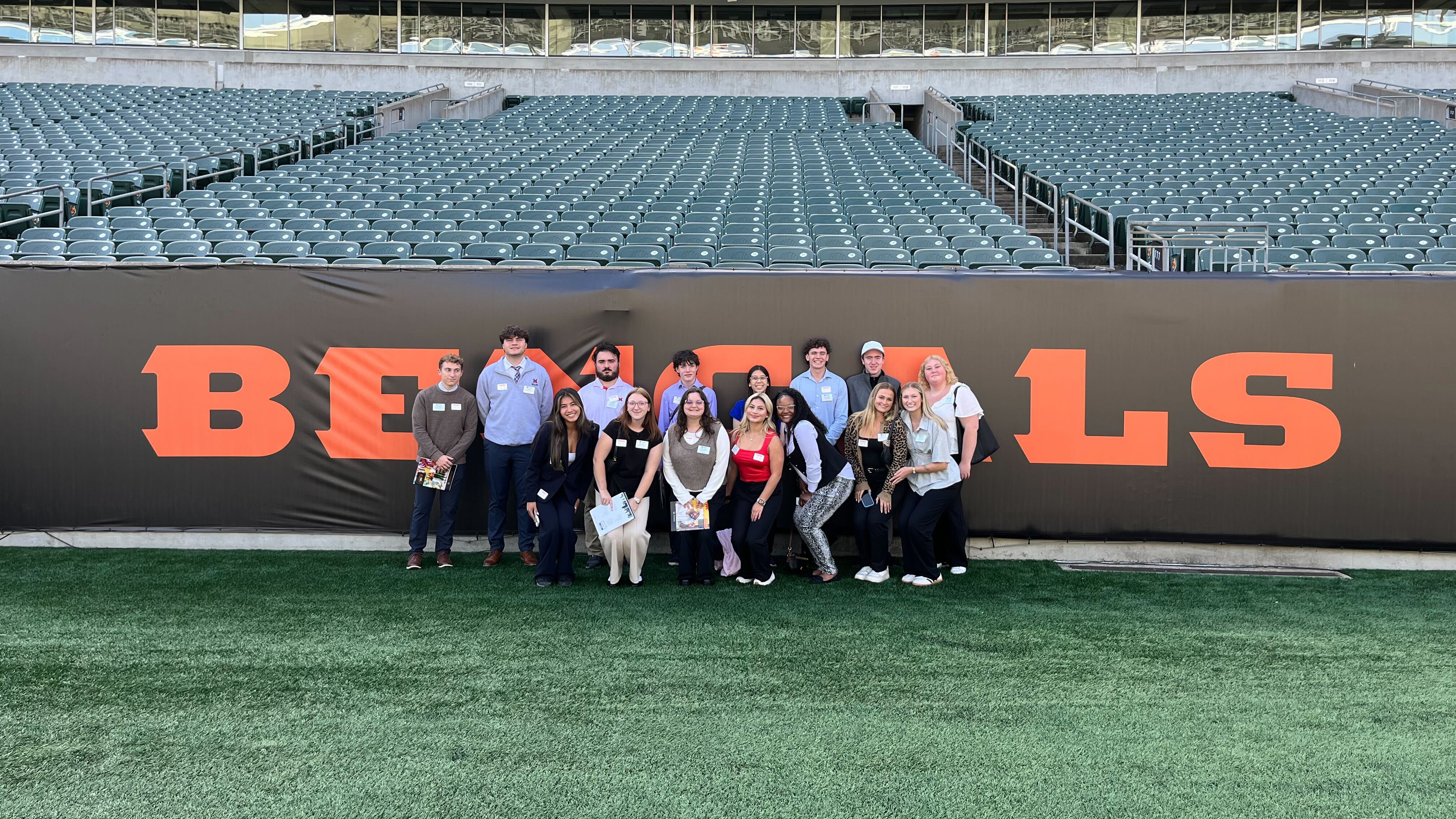 A group of students pose in front of a Bengals word mark on the field at Paycor Stadium.