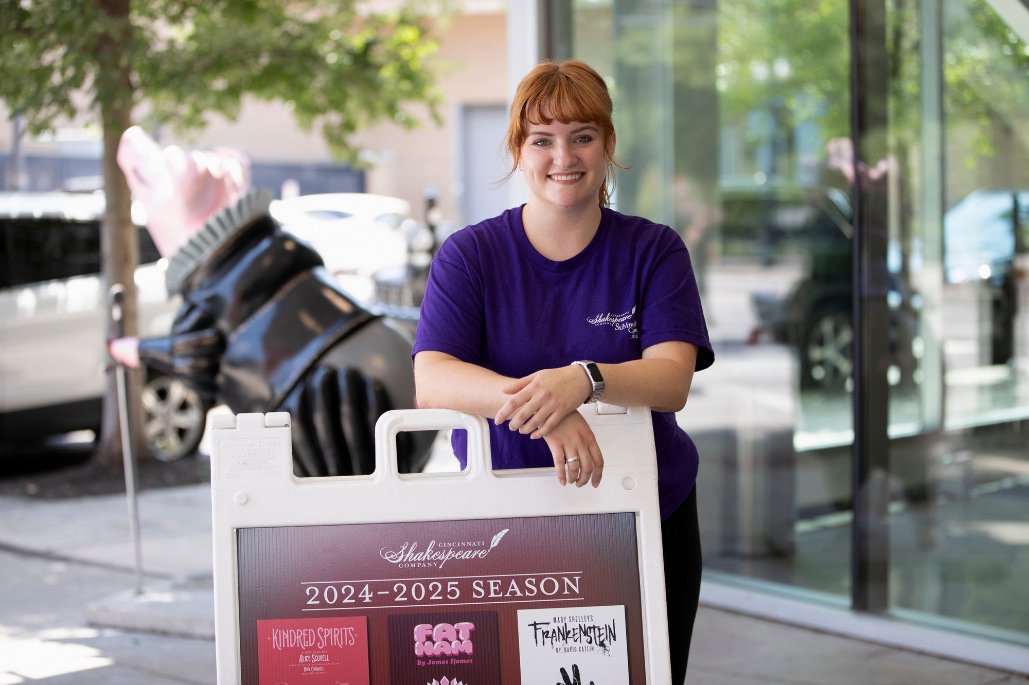 A student intern poses with a Cincinnati Shakespeare Company season sign.