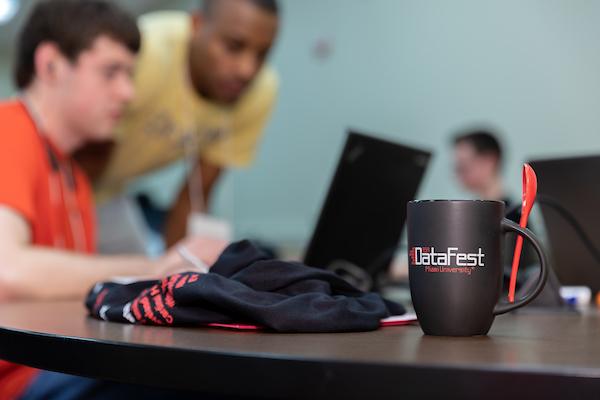 A mug with the DataFest logo and people working on a computer in the background.