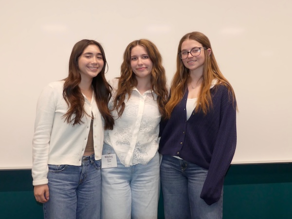 The body is t-test team standing together and smiling in front of a projector screen.