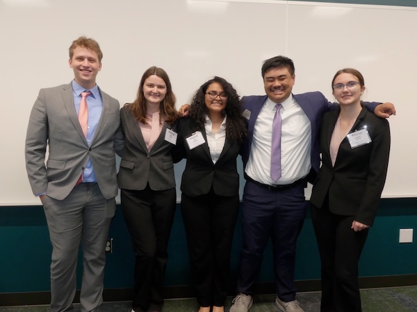 The significant figures team standing in business attire and smiling in front of a whiteboard.