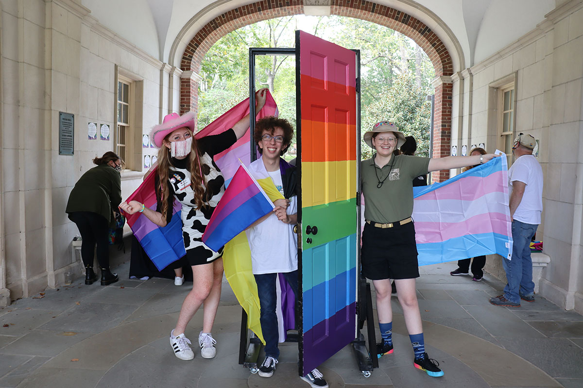 Three students standing in front of a rainbow door.