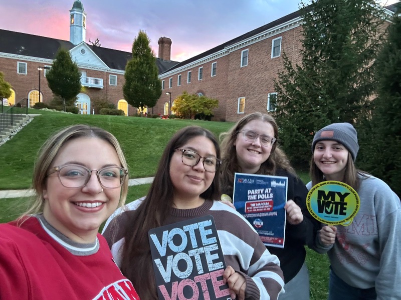 A group of four young people holding up votin signs on campus.