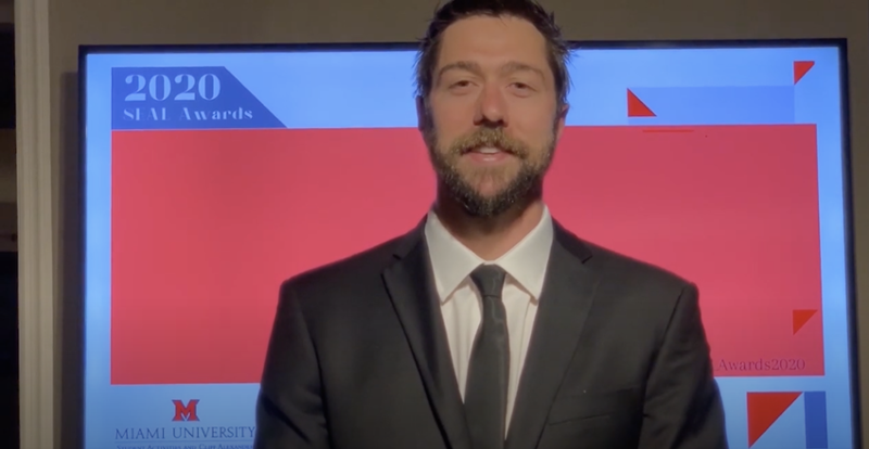 Drew Davis of Student Activities, in a suit and tie, presenting in front of a screen